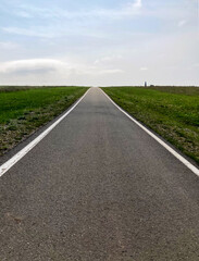 A straight asphalt road passing through green fields under moody sky