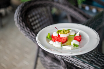 Elegant gourmet appetizer with watermelon, green puree, cheese, and herbs artfully arranged on a white plate, showcasing fine dining and creative culinary presentation.