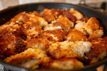 Close-up view of golden brown breaded chicken being fried in a black pan on a gas stove. The crispy coating and sizzling oil suggest the dish is almost ready to serve. High quality photo