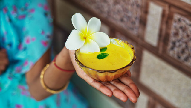 One female hand holding homemade facial in bowl. Ayurvedic face pack of Haldi (Turmeric), Rose water and leaves. mortar of Ubtan for skincare. Natural way for skin beauty using since ancient India