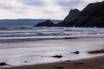 Waves of the incoming tide with the cliffs of the Welsh coast in the background in the late...