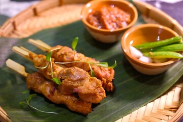 Grilled chicken skewers on banana leaf with spicy dipping sauces and vegetables