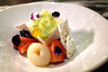 Elegant plated dessert with green tea ice cream, fresh strawberries, lychee, and floral garnish