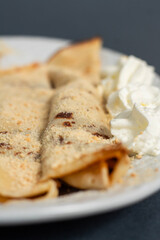 Delicious rolled pancakes served on a plate with whipped cream and ground biscuit on a gray textured surface 