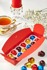 Colorful wrapped chocolates in red box with teacup and candle