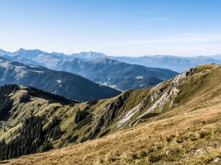 Fototapeta premium Breathtaking view of mountain ranges covered in lush greenery under a clear blue sky. The wide panoramic scene captures nature’s beauty and tranquility, perfect for use in travel, nature, adventure