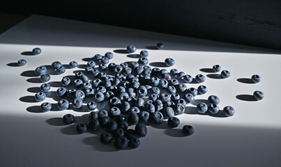 Blueberries scattered on a white table in a beam of light.