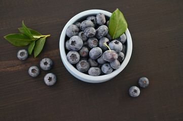 Blueberries with green leaves in a blue cup on a dark wooden background.
