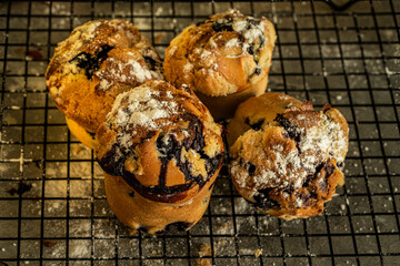 Delicious French muffins or blueberry muffins sprinkled with powdered sugar on a black wire rack. Close-up.