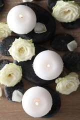 Burning candles, stones and rose flowers on wooden table, flat lay