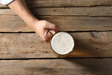 Man with glass mug of beer at wooden table, top view