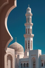 Fototapeta premium A sunlit, off-white mosque's minaret and dome are partially framed by a carved stone archway against a vivid blue sky