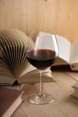Glass of red wine and books on wooden table, closeup
