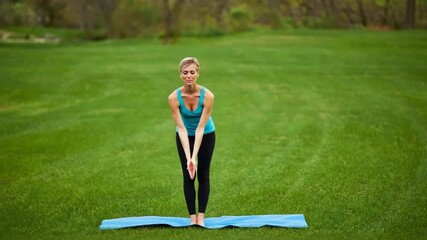 Woman performs yoga pose on mat in a green park during sunny day - Powered by Adobe