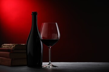 Tasty wine and stacked books on dark textured table in red light, closeup