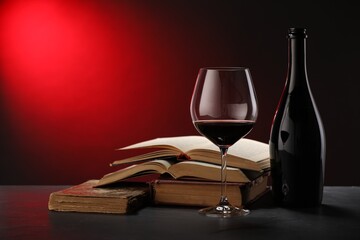 Tasty wine and stacked books on dark table in red light, closeup