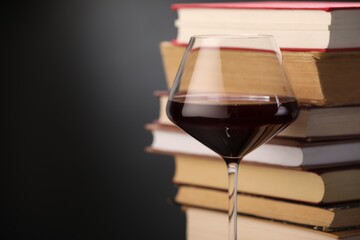 Red wine in glass and stack of books on dark background, closeup. Space for text