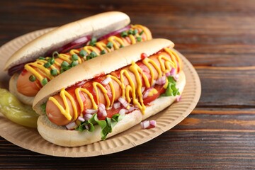 Delicious hot dogs with sauces, lettuce and onion on wooden table, closeup