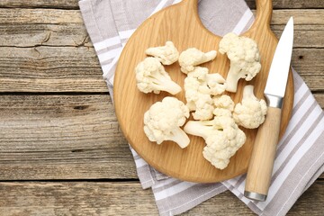 Fresh raw cauliflower florets and knife on wooden table, top view. Space for text
