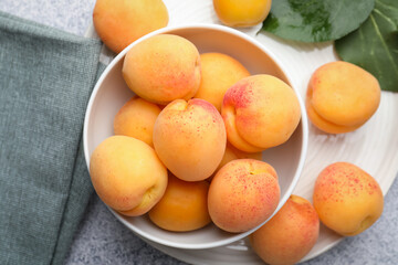 Fresh apricots in bowl and green leaves on grey textured table, flat lay