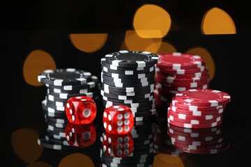Casino chips and dice on mirror surface against blurred lights, closeup