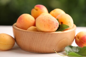 Fresh ripe apricots in bowl on white wooden table outdoors, closeup