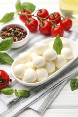 Tasty mozzarella cheese, tomatoes, basil and spices on white wooden table, closeup