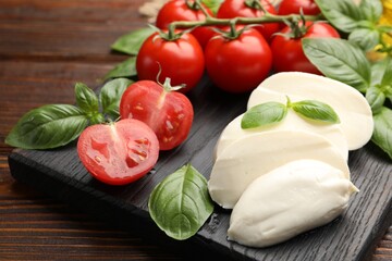 Tasty mozzarella cheese, tomatoes and basil on wooden table, closeup