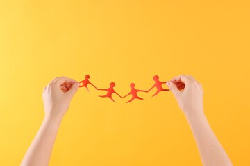 Woman holding paper figures of people on orange background, closeup