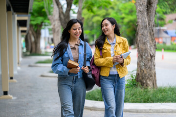 Two happy asian students walking and talking on university campus