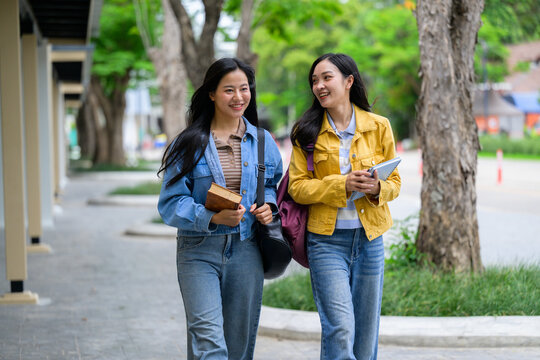 Two happy asian students walking and talking on university campus