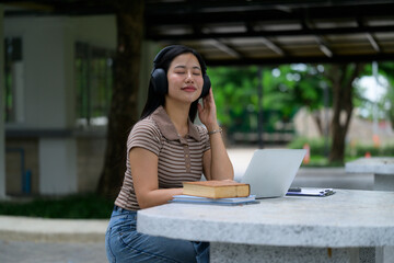 Obraz premium Young Asian student listening to music with headphones while studying outdoors