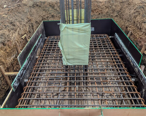 Steel reinforcement for concrete column and footing at construction site, showing detailed rebar arrangement and formwork before concrete pouring.
