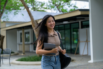 Young asian student walking outdoors carrying tablet and bag