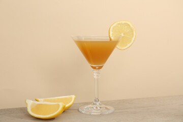 Tasty lemon cocktail in glass and fresh fruit pieces on wooden table against beige background