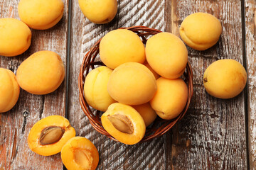Fresh ripe apricots in wicker basket on wooden table, flat lay