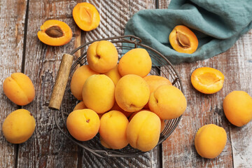 Fresh ripe apricots in metal basket on wooden table, flat lay