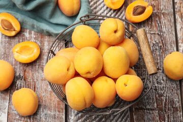 Fresh ripe apricots in metal basket on wooden table, flat lay