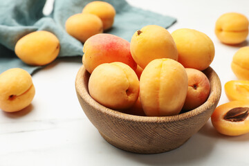 Fresh ripe apricots in bowl on white marble table, closeup