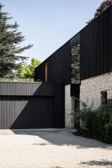 Fototapeta premium Modern architecture features a sleek black exterior and stone accents, surrounded by greenery, showcasing a unique design in a serene outdoor setting