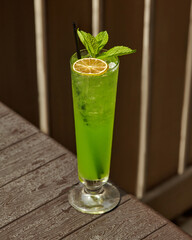 Refreshing green cocktail sitting on wooden table with lime and mint garnish