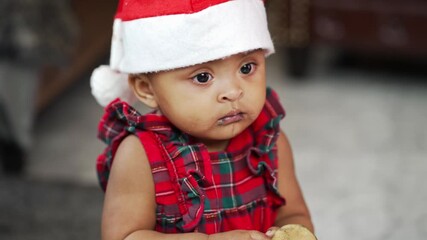 African baby girl in santa claus costume holding cookie on floor - Powered by Adobe