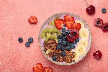 Vibrant and nutritious acai bowl topped with sliced kiwi, strawberries, blueberries, cherries, banana, and granola, a colorful and healthy meal or breakfast on a pink background