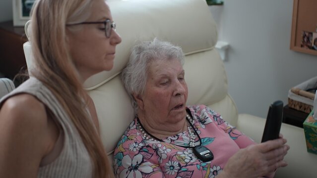 An elderly mother receives help from her daughter to learn how to use the telephone during a visit at a senior living facility.