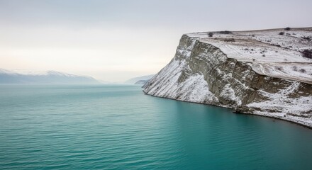 Majestic turquoise sea meets snow-covered cliffs under a serene winter sky offering a remote and