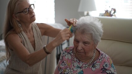 A mature woman thoughtfully brushes her elderly mothers hair while sitting in a comfortable living room during a warm afternoon visit filled with care and tenderness.