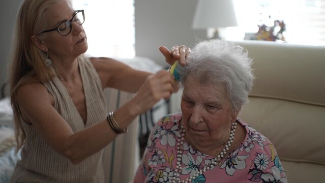 A mature woman thoughtfully brushes her elderly mothers hair while sitting in a comfortable living room during a warm afternoon visit filled with care and tenderness.