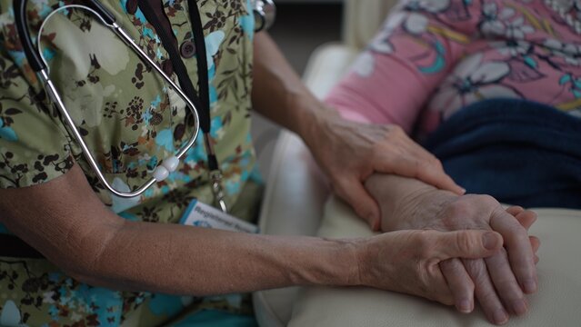 A nurse provides comfort to an elderly woman by holding her hand during a hospital visit, fostering connection and care in a compassionate setting.