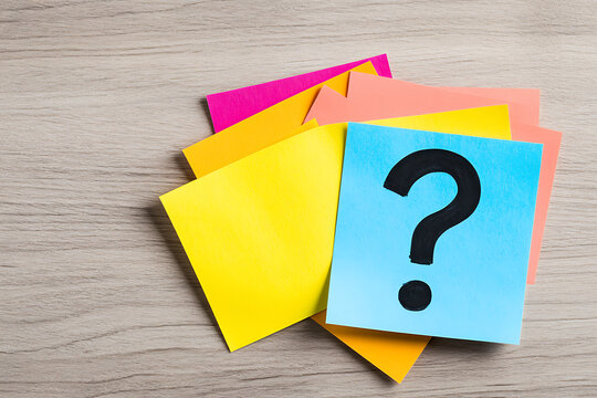 Colorful sticky notes on a wood surface, featuring a question mark. Focus on inquiry, reminders, and vibrant office supplies.