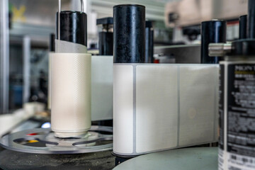 Industrial labeling machine with a roll of blank white labels on a factory assembly line. Close up of automated equipment for packaging. Concept of manufacturing and modern industrial technology.